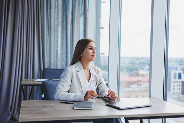 Successful young female manager in an elegant casual jacket and optical glasses, sits in the office at the workplace, an experienced woman with a modern laptop, working in the office - Photo, image
