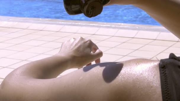 Een vrouw die geniet van de zon op een zonnige dag bij het zwembad, zonnebrandolie op haar huid aanbrengend, in slow motion - Video