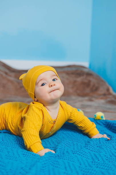 Un bambino piccolo di 4-5 mesi giace su un letto in abiti gialli. Il bambino comincia a tenere la testa. Vestiti per bambini - Foto, immagini