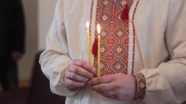 Man holds two candles in a temple in a traditional Ukrainian dress at christening - Footage, Video