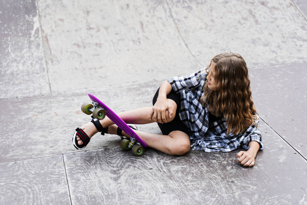 Leg and knee injury on penny board. Child traumatology. Child girl falling from skate board and get injured and feeling pain - Foto, afbeelding
