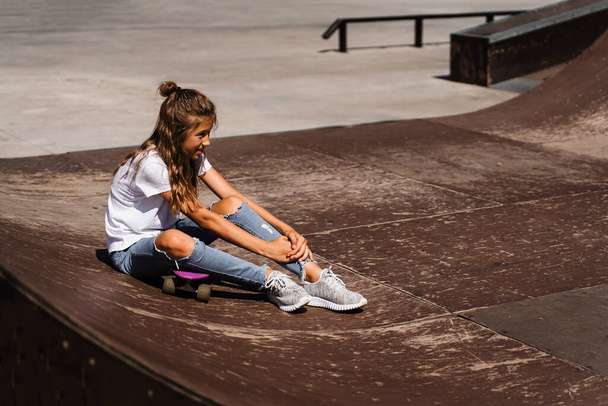 Aktywne dziecko dziewczyna po upadku z tablicy groszowej rannych, siedzi i czuje ból na rampie sportowej na placu zabaw skate park - Zdjęcie, obraz