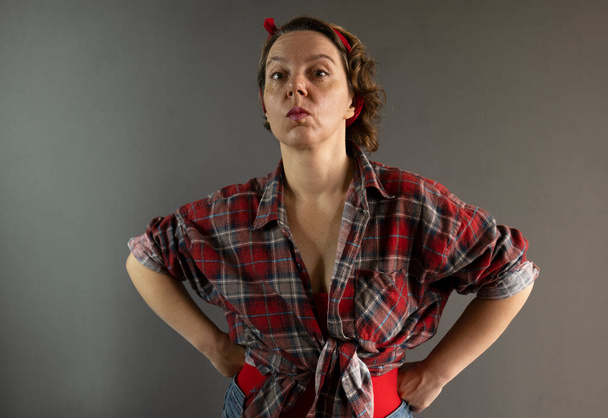 Forty-year-old pin-up woman in a plaid shirt on a gray background. Portrait of a strict woman. Adult serious pin-up woman - Foto, Imagem