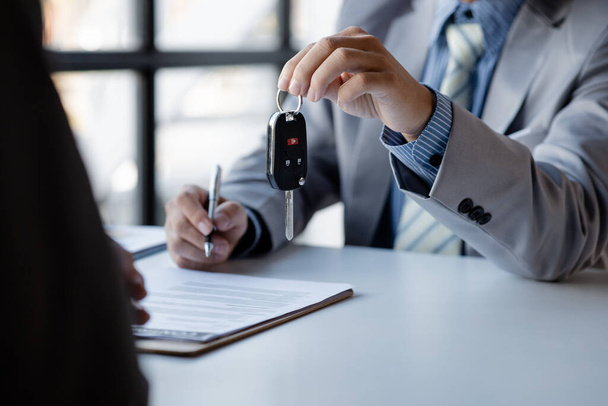 The car salesman hands the key to the customer after discussing the details and signing the purchase agreement, selling the car, selling the car from a major dealer. Vehicle sales concept. - Foto, afbeelding