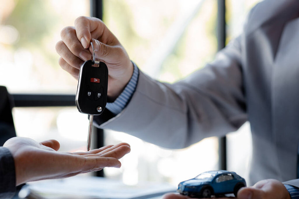 The car salesman hands the key to the customer after discussing the details and signing the purchase agreement, selling the car, selling the car from a major dealer. Vehicle sales concept. - Foto, Bild