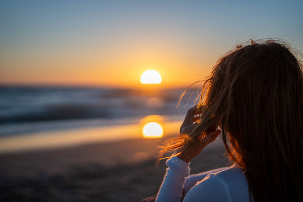 Rear view of a red-haired woman talking on her cell phone while watching the sunset over the ocean - Fotoğraf, Görsel