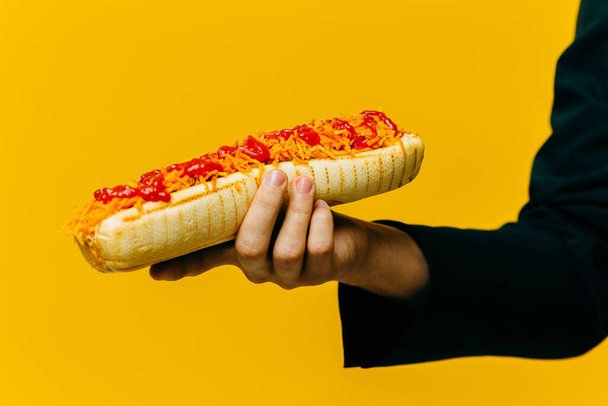 Hot dog w ręku z bliska. Studio zdjęcie na kolorowym tle, przestrzeń do kopiowania. - Zdjęcie, obraz