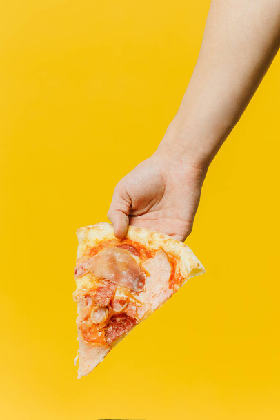 Een stuk pizza in de hand. Studio foto op een gekleurde achtergrond, kopieer ruimte. - Foto, afbeelding