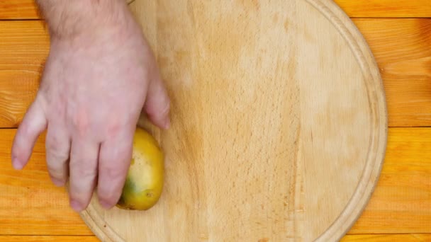 The cook is preparing to peel the potatoes. A man lays out raw fresh potatoes and a manual potato peeler. Unpeeled potatoes on a cutting board on a wooden table. Cooking food. Close-up. Top view - Video, Çekim
