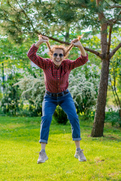 Smějící se žena visí ve vzduchu a drží se za dva copánky v zeleném parku. Blázníš jako dítě.. - Fotografie, Obrázek