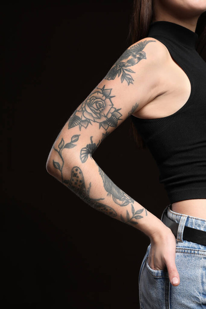Beautiful woman with tattoos on arm against black background, closeup - Foto, imagen