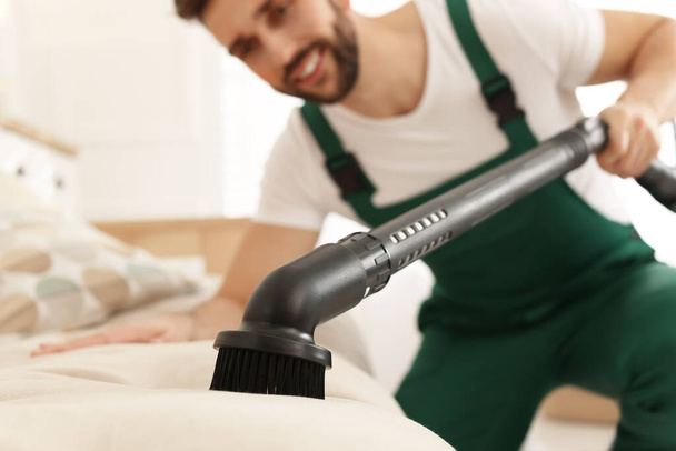 Professional janitor vacuuming sofa in living room, focus on nozzle - Фото, зображення