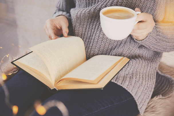 Женщина с чашкой кофе читает книгу дома, крупным планом
 - Фото, изображение