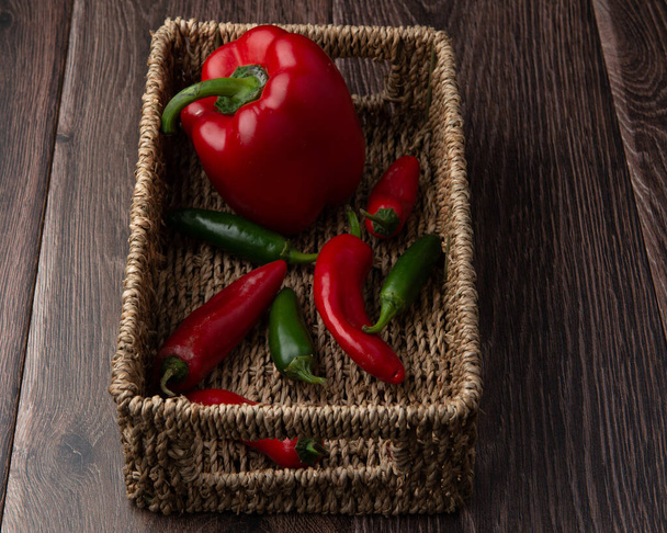 Red pepper and chillies in a basket on a dark wood background - Foto, imagen