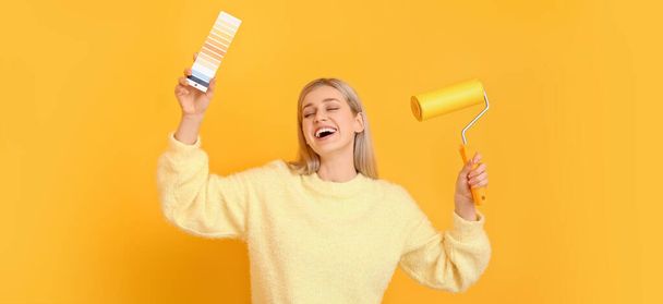 Beautiful young woman with color palettes and paint roller on yellow background  - Foto, Imagen
