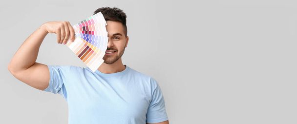 Handsome young man holding color palettes on light background with space for text - Φωτογραφία, εικόνα