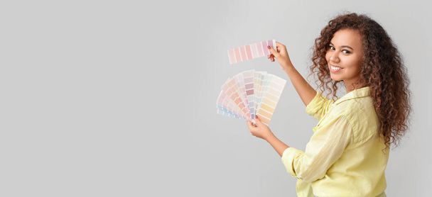 Beautiful young African-American woman holding color palettes on light background with space for text - 写真・画像
