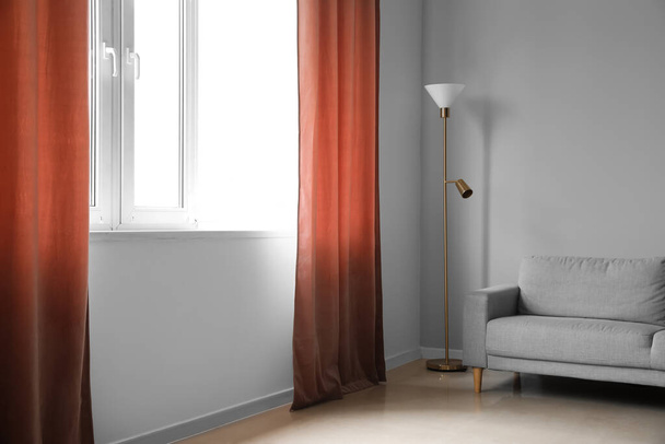 Szürke kanapé és standard lámpa közelében piros függöny a szobában - Fotó, kép