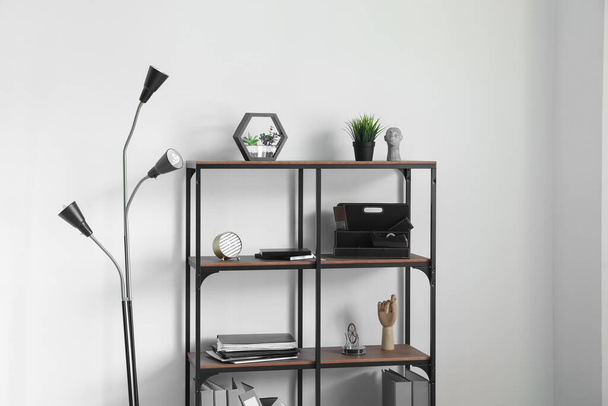 Shelving unit with office stuff and lamp near light wall - Foto, imagen