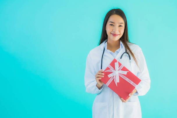 Retrato hermosa joven asiática médico mujer con caja de regalo en azul aislado fondo
 - Foto, imagen