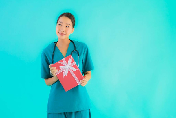 Retrato bonito jovem asiático médico mulher mostrar vermelho dom caixa no azul isolado fundo
 - Foto, Imagem