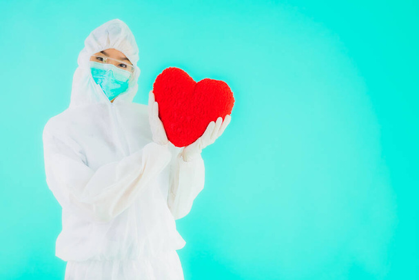 Retrato hermosa joven asiática médico mujer usar ppe o equipo de protección personal para proteger de coronavirus o covid19 mostrar el corazón en azul aislado fondo
 - Foto, imagen