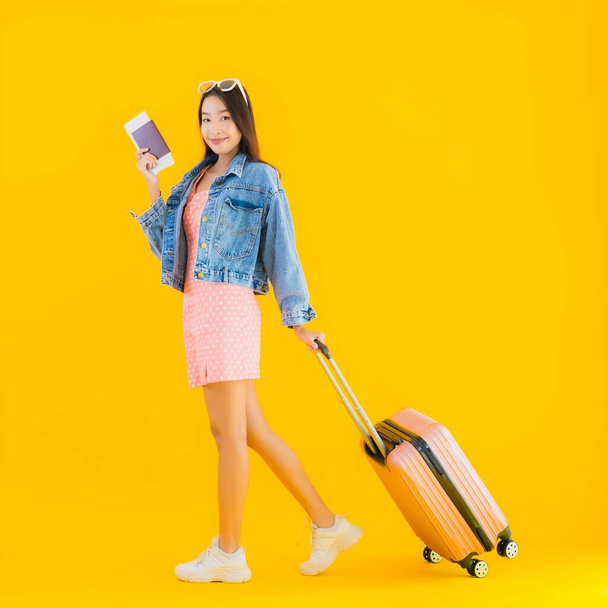 Retrato hermosa joven asiática mujer con equipaje bolsa de viaje con pasaporte y billete de embarque en amarillo aislado fondo
 - Foto, Imagen
