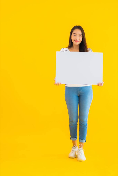 Портрет красивая молодая азиатская женщина показывают пустой белый рекламный знак на желтом изолированном фоне
 - Фото, изображение