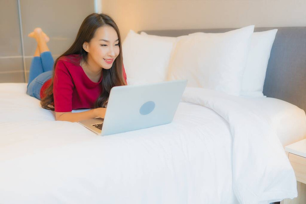Portret mooie jonge aziatische vrouw gebruik laptop computer op bed in slaapkamer interieur - Foto, afbeelding