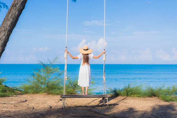 retrato hermosa joven asiático mujer relax sonrisa en swing alrededor playa mar océano para naturaleza viaje en vacaciones - Foto, Imagen