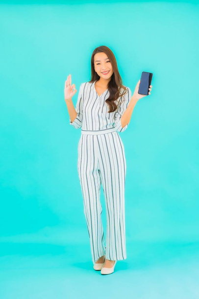 Портрет красива молода азіатка використовує смартфон на синьому фоні
 - Фото, зображення