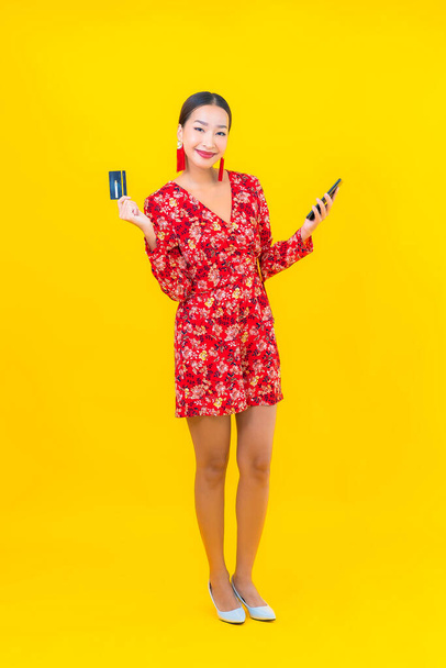 ポートレート美しい若いアジアの女性は黄色の色の背景にスマートフォンを使用します - 写真・画像