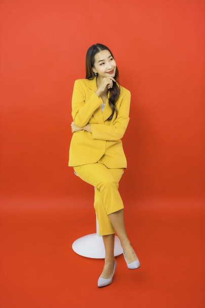 Retrato bonito jovem negócio asiático mulher sentar na cadeira com sorriso no fundo vermelho - Foto, Imagem