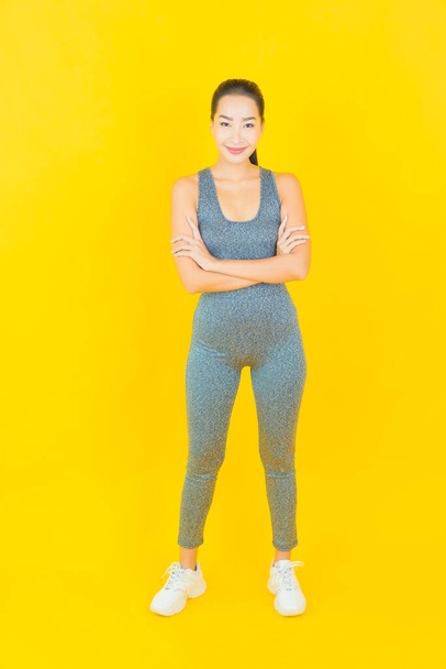 Portret mooie jonge aziatische vrouw met sportkleding klaar voor oefening op gele achtergrond - Foto, afbeelding