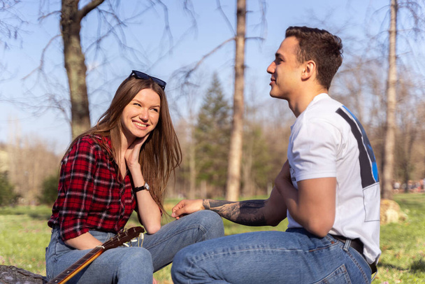 Cute girl laughing at her boyfriend while they are sitting in the park - Fotoğraf, Görsel