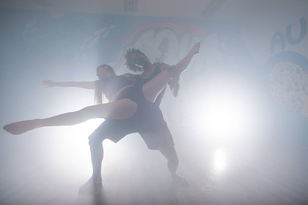 Група багаторасових танцюристів насолоджується фанк хіп-хоп рухами в темній студії з димом і освітленням. Група молодих хіп-хоп танцюристів виступає на сцені. Щасливі жінки танцюють
. - Фото, зображення