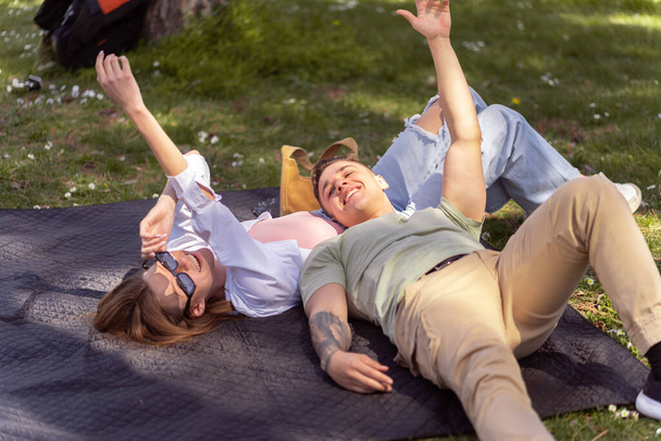 Unique perspective of two teenage friend while lying down on green meadow. Enjoying in spring time - Photo, Image