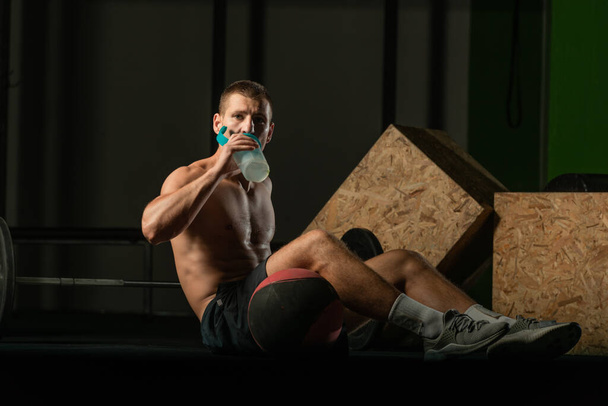 Nuori lihaksikas mies juo proteiinipirtelöä treenaamisen jälkeen sisätiloissa. - Valokuva, kuva