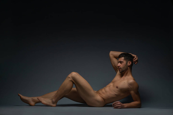 Мода обнаженная фотография мужчины модели с соблазнительной фигурой, лежащей изолированно на полу в студии - Фото, изображение