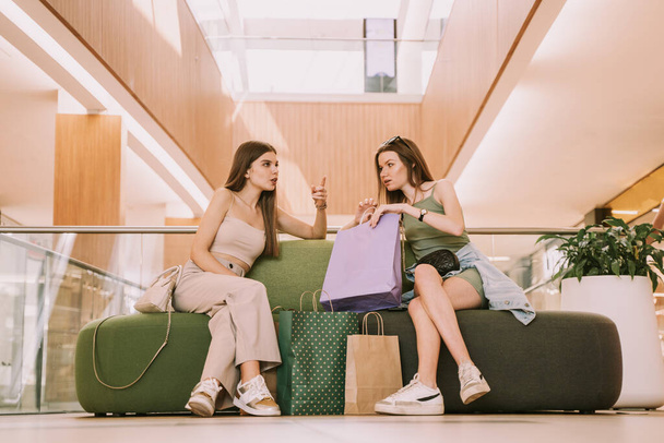 Двое лучших друзей в торговом центре смотрят на сумки, сидя на диване - Фото, изображение