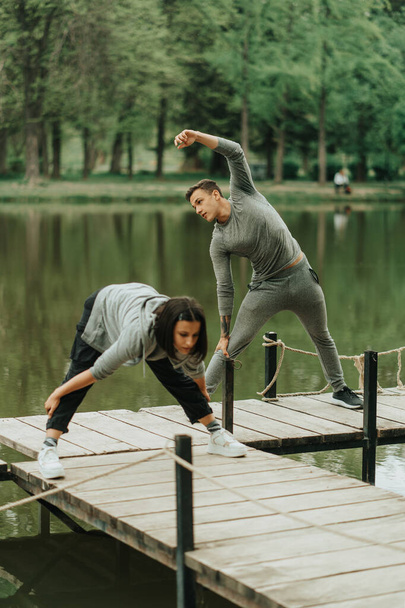 Hermosa pareja haciendo ejercicio en el puente cerca del lago en el parque - Foto, Imagen