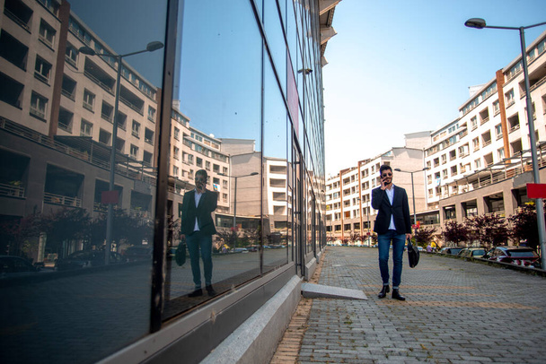 Businessman talking on the phone while walking near the building - Fotó, kép
