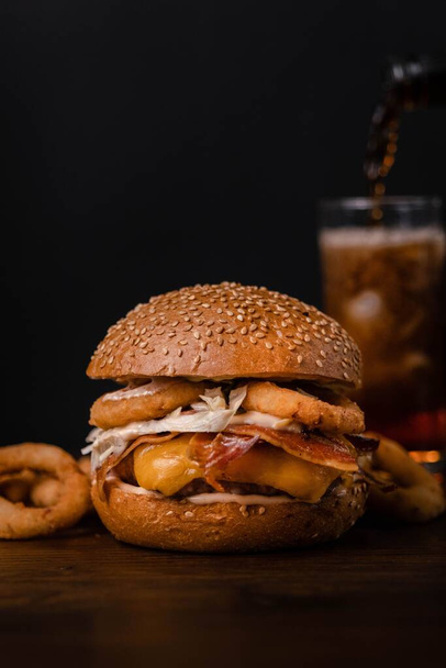 A vertical shot of a hamburger with different ingredients on a wooden table in a blurred background - Foto, immagini