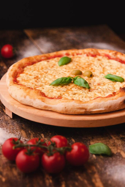 A vertical shot of a tasty pizza with cheese and olives and cherry tomatoes on a wooden table - Foto, afbeelding
