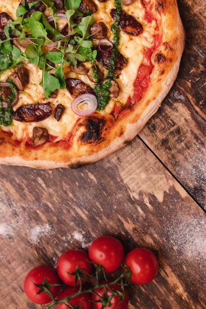 A vertical shot of a tasty and crusty pizza with vegetables and cherry tomatoes on a wooden table - Photo, Image
