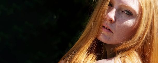 closeup wide banner portrait of beautiful redhead woman, in the summer sun, looking seductively sensual over her shoulder on the side of the picture, copy space - Photo, image