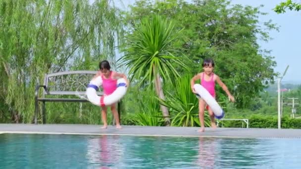 Šťastné sestřičky s gumovým kroužkem v bazénu. Děti si během rodinné letní dovolené hrají ve venkovním bazénu tropického letoviska. Děti se učí plavat. Zdravé letní aktivity pro děti. - Záběry, video