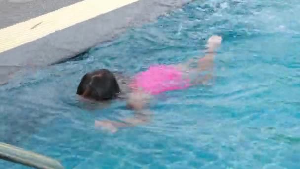 Happy little girl is swimming and playing in outdoor swimming pool in a tropical resort during family summer vacation. Girl learning to dive and swim. Healthy Summer Activities for Kids. - Felvétel, videó