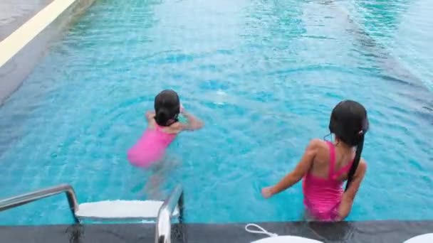 Szczęśliwe siostrzyczki pływają i bawią się w odkrytym basenie w tropikalnym kurorcie podczas rodzinnych wakacji letnich. Dzieci uczą się nurkować i pływać. Zdrowe zajęcia letnie dla dzieci. - Materiał filmowy, wideo