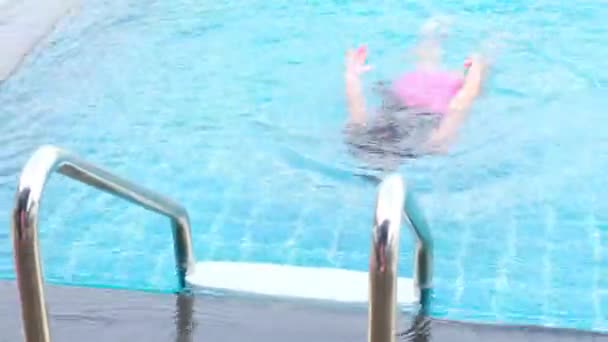 Happy little girl is swimming and playing in outdoor swimming pool in a tropical resort during family summer vacation. Girl learning to dive and swim. Healthy Summer Activities for Kids. - Filmagem, Vídeo